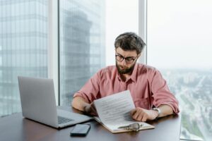 Professional man in pink shirt working with documents at a modern office desk.